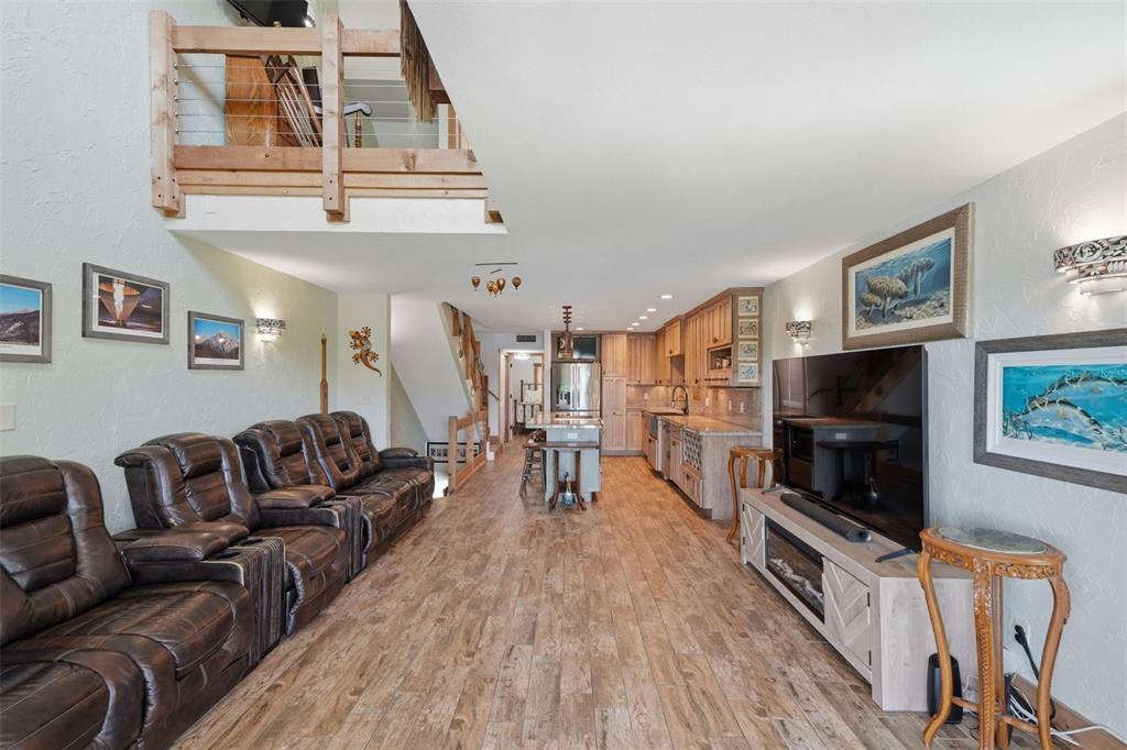 An open-concept living room and kitchen with wood-look tile flooring and a lofted balcony — 1375 PINELLAS BAYWAY S UNIT 39, TIERRA VERDE, FL