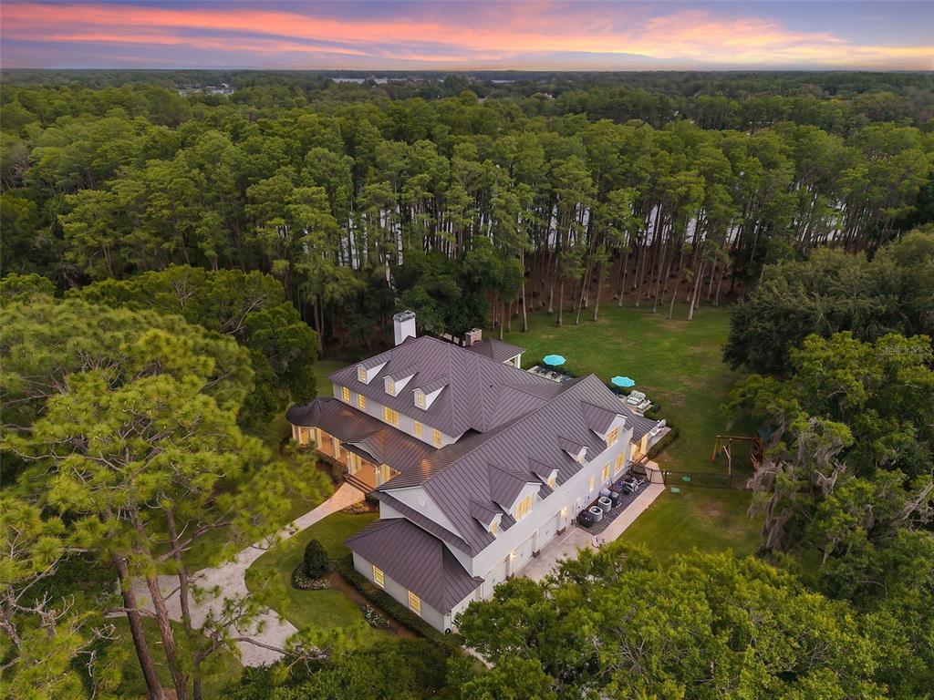 An aerial view of a large house with a dark metal roof surrounded by trees — 18562 COUNCIL CREST DRIVE, ODESSA, FL