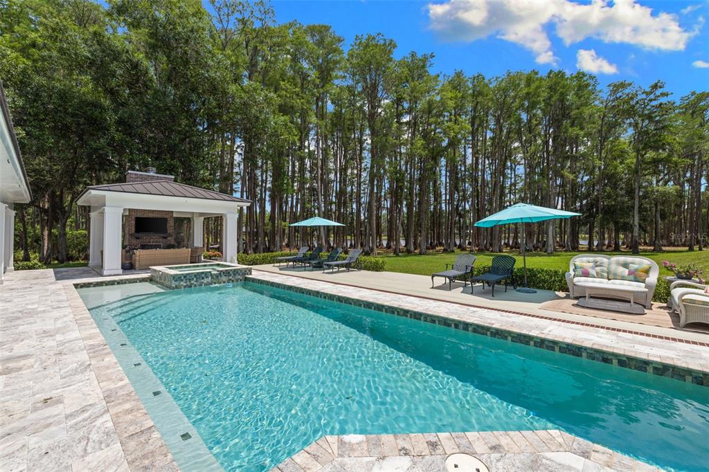 A swimming pool and hot tub sit on a stone patio beside a covered pavilion — 18562 COUNCIL CREST DRIVE, ODESSA, FL