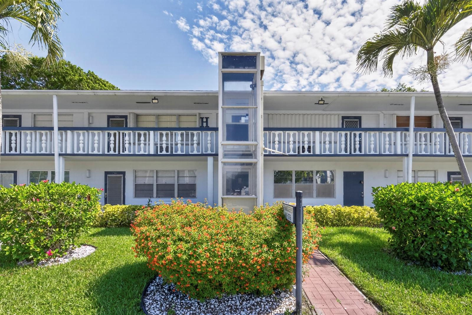 A two-story apartment building features a central glass elevator shaft and a white balcony railing — 176 Upminster H # 176, Deerfield Beach FL 33442, DEERFIELD BEACH, FL