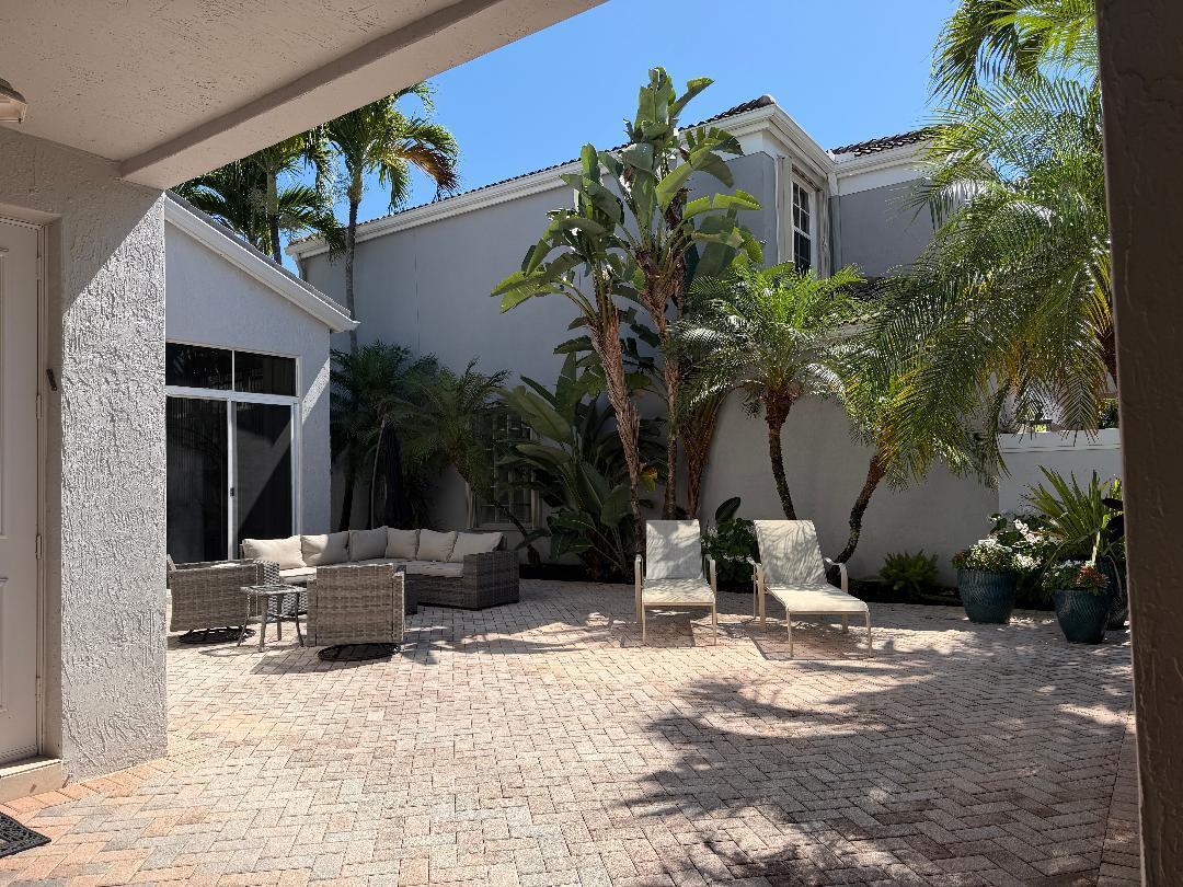 A paved patio features outdoor lounge furniture, sun loungers, and tropical plants against a house exterior — 4285 NW 62nd Road, Boca Raton FL 33496, BOCA RATON, FL