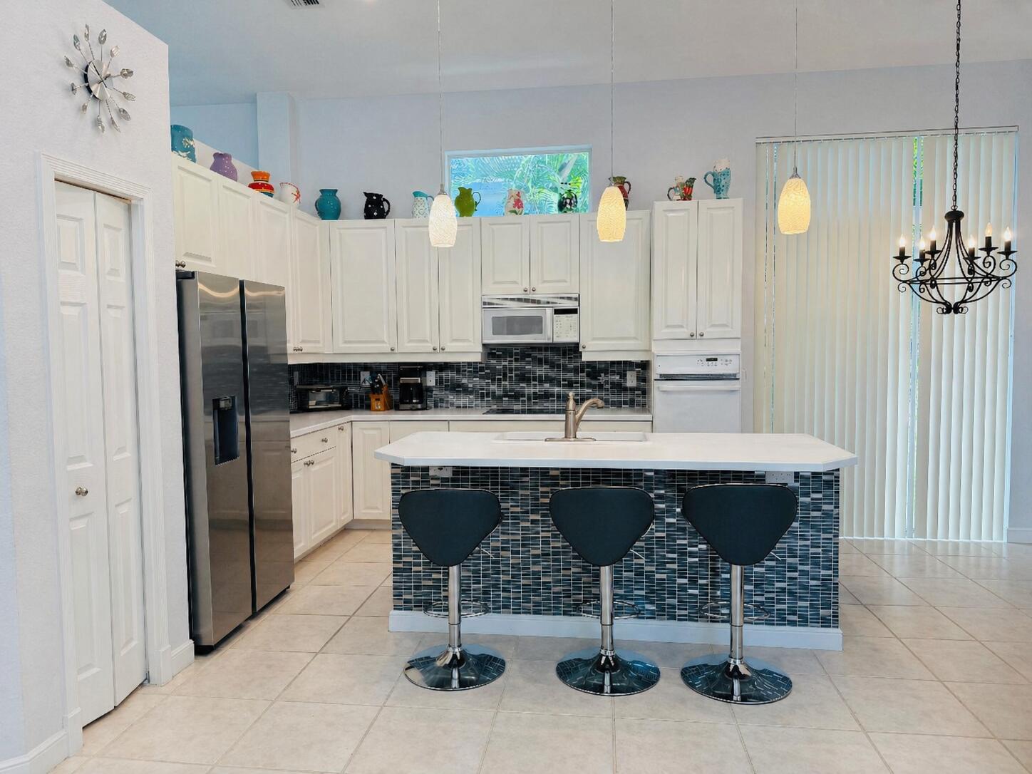 A kitchen features white cabinets, stainless steel appliances, a tiled island, and three bar stools — 4285 NW 62nd Road, Boca Raton FL 33496, BOCA RATON, FL