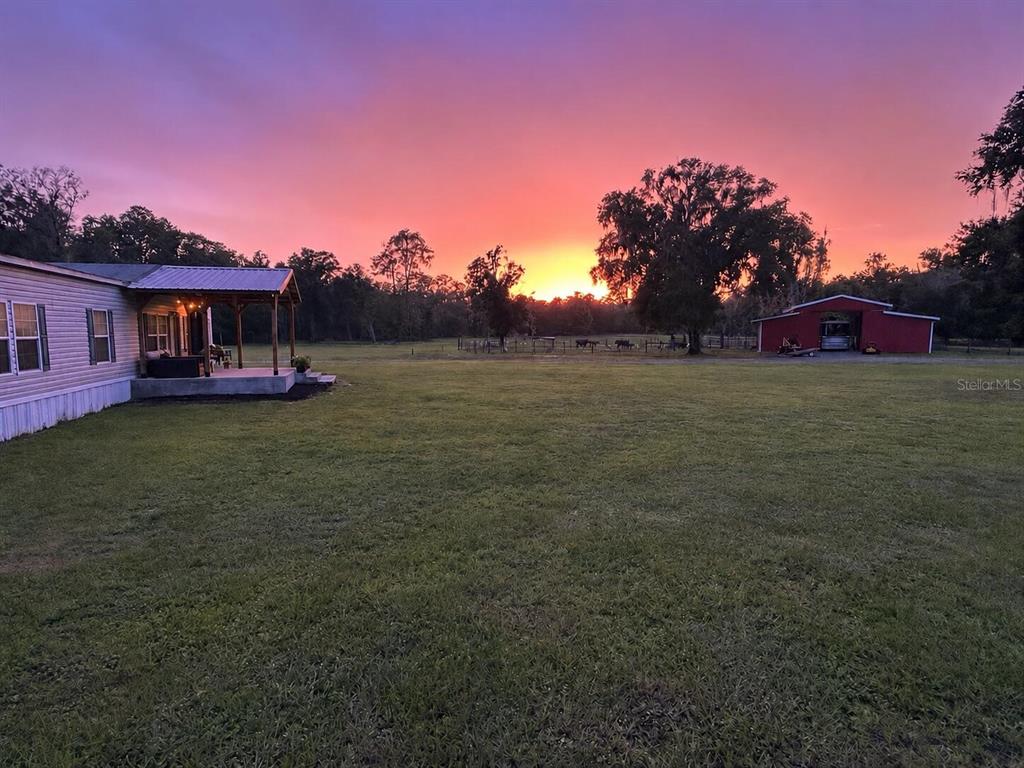 A house with a porch and a red barn sit on a grassy field at sunset — 12275 LAKELAND ACRES, LAKELAND, FL