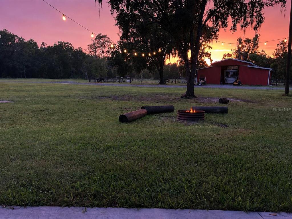 A fire pit sits in a grassy yard at sunset near a red barn — 12275 LAKELAND ACRES, LAKELAND, FL
