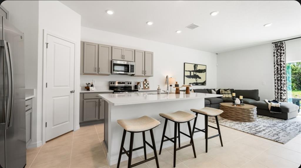 A modern open-concept kitchen features a white island, gray cabinetry, and an adjacent living area — 10814 ECLIPSE STREET, SARASOTA, FL