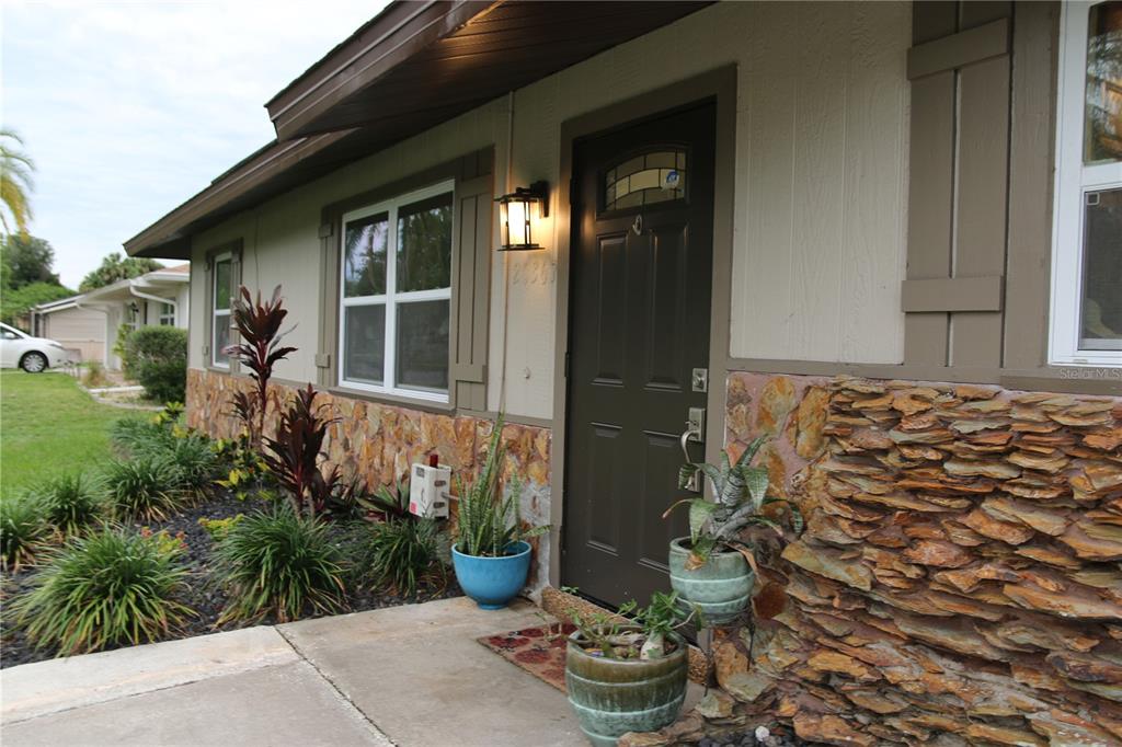 The exterior of a house features a brown front door, stone siding, and potted plants — 20367 ANDOVER AVENUE, PORT CHARLOTTE, FL