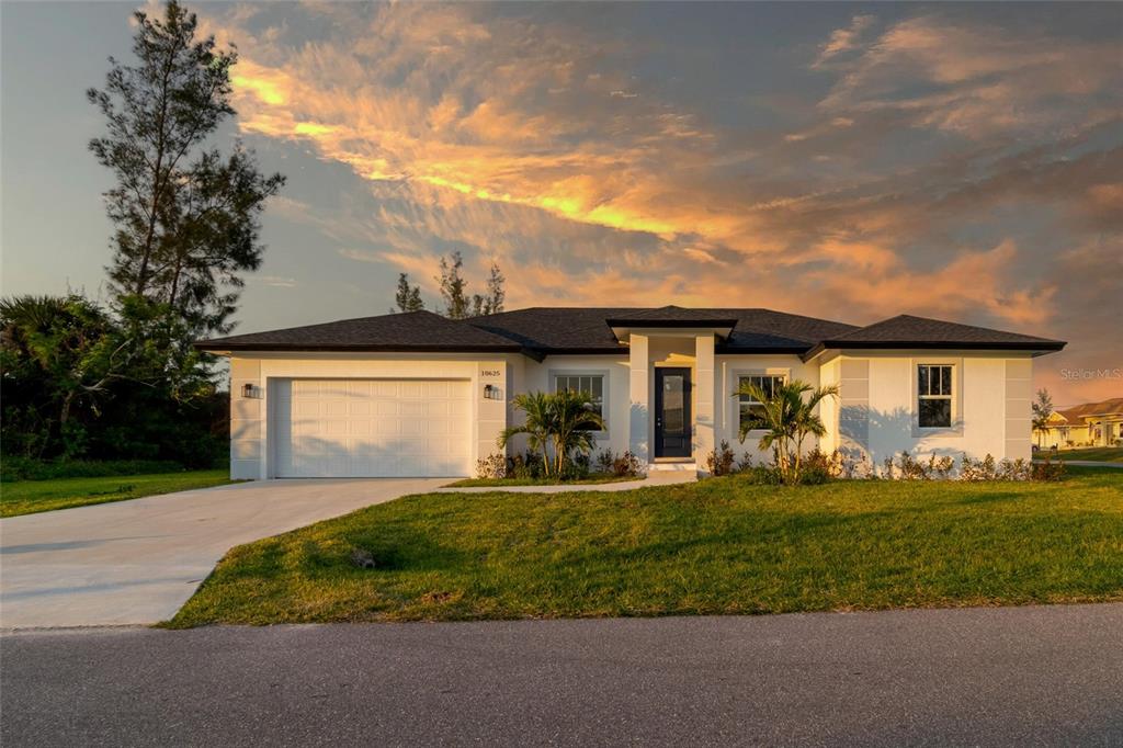 A single-story white house with a two-car garage and a paved driveway at sunset — 10625 AYEAR ROAD, PORT CHARLOTTE, FL