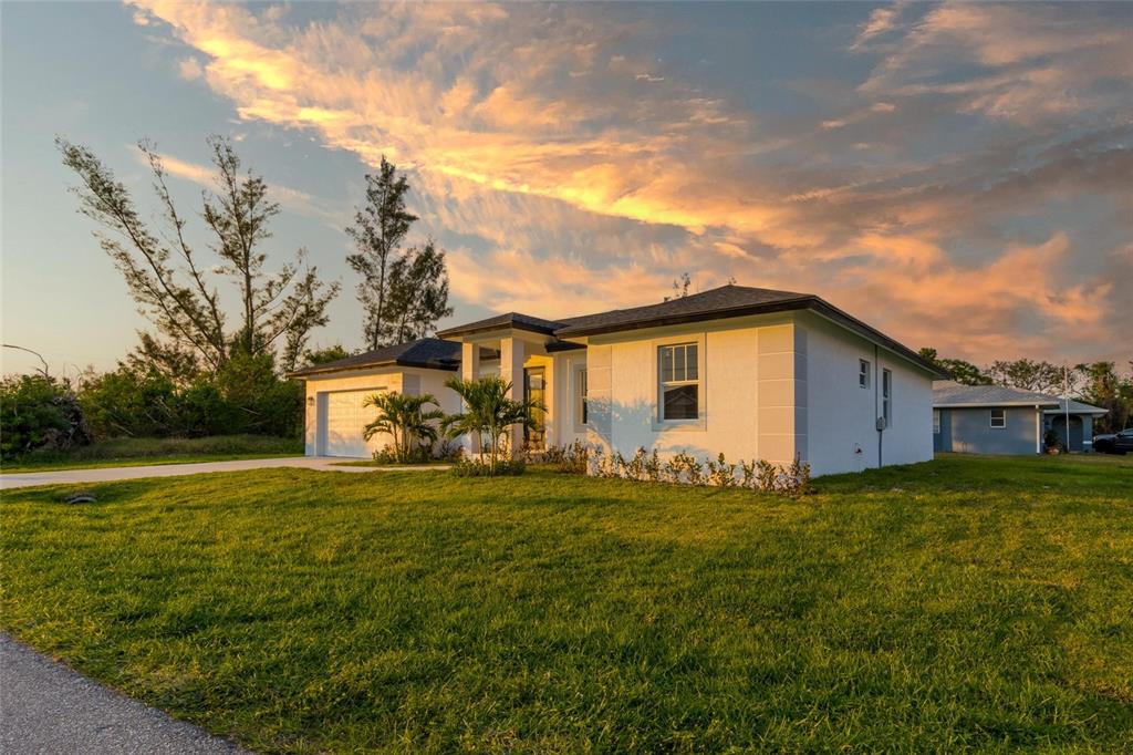 A white single-story house with a garage and palm trees under a sunset sky — 10625 AYEAR ROAD, PORT CHARLOTTE, FL