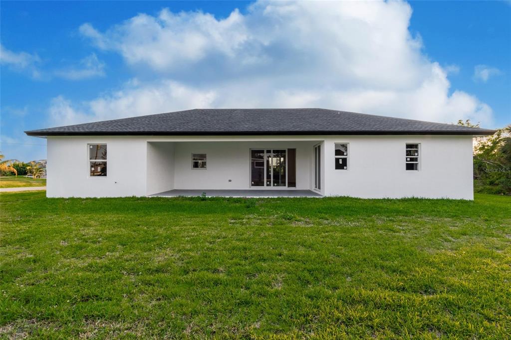 The rear exterior of a white, single-story house features a covered patio and lawn — 10625 AYEAR ROAD, PORT CHARLOTTE, FL