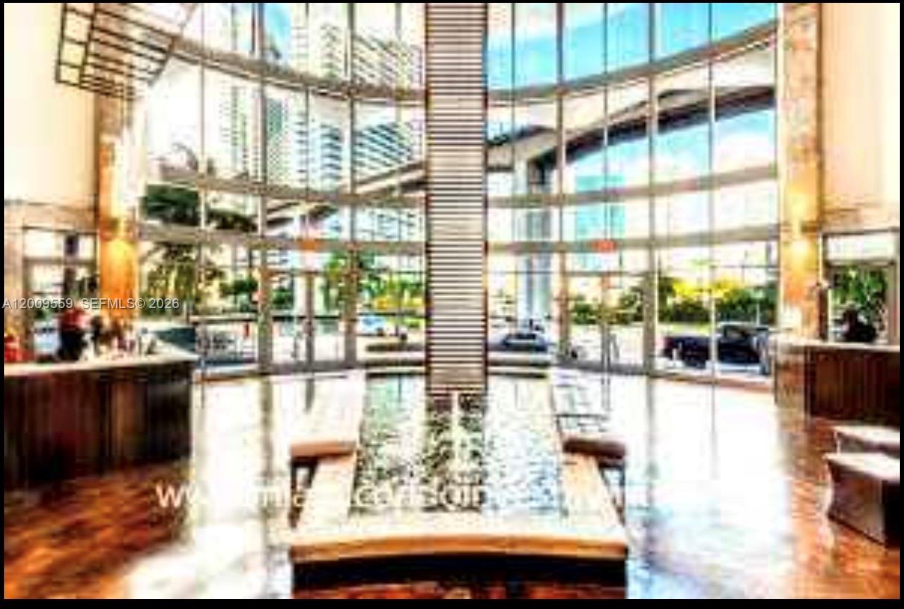 A modern building lobby features floor-to-ceiling windows, a central water feature, and wood flooring — 690 SW 1st Ct, Miami FL 33130, MIAMI, FL