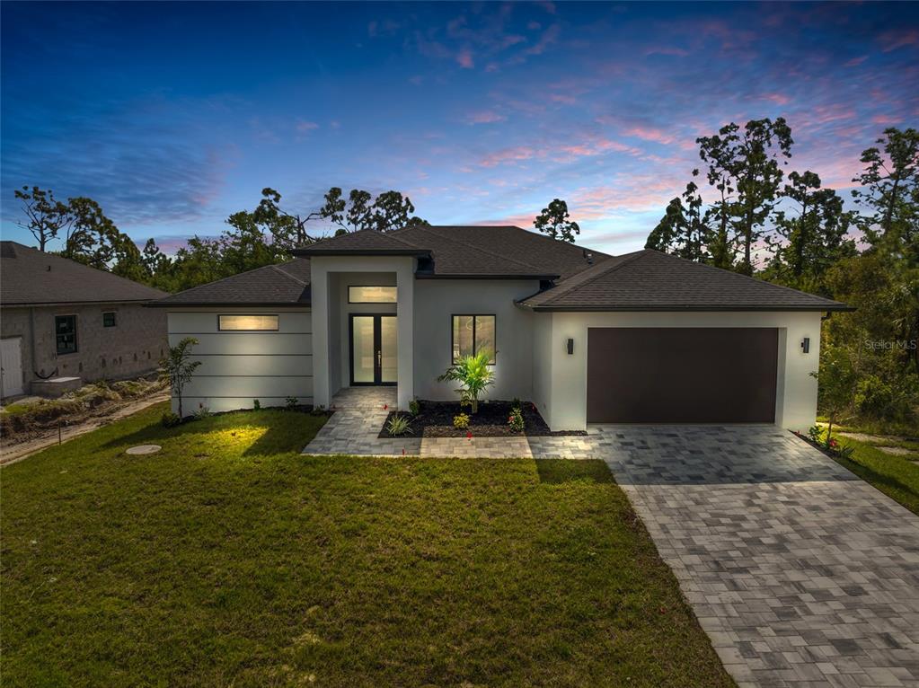 A modern single-story house with a paved driveway, dark garage door, and a landscaped yard — 9108 SANTA LUCIA DRIVE, PORT CHARLOTTE, FL