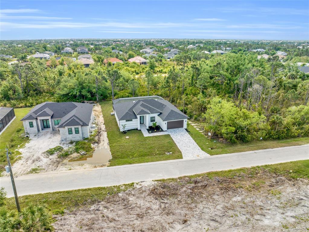 An aerial view shows two single-story houses with dark roofs situated along a paved road — 9108 SANTA LUCIA DRIVE, PORT CHARLOTTE, FL