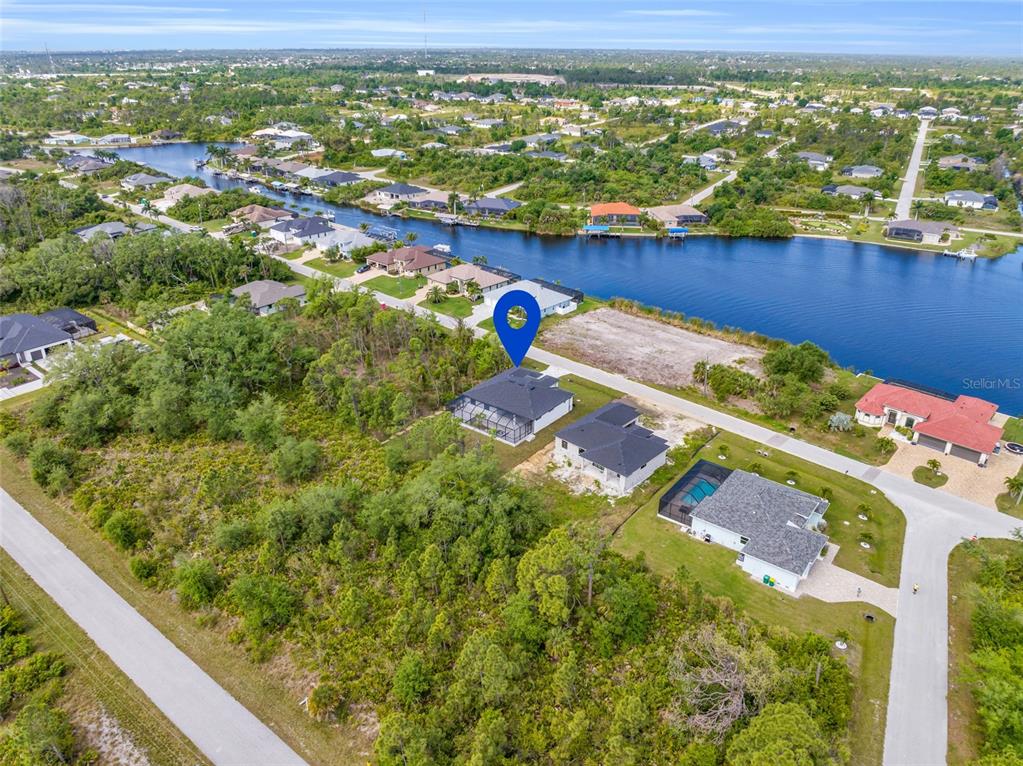 An aerial view shows a house with a pool cage near a canal and woods — 9108 SANTA LUCIA DRIVE, PORT CHARLOTTE, FL