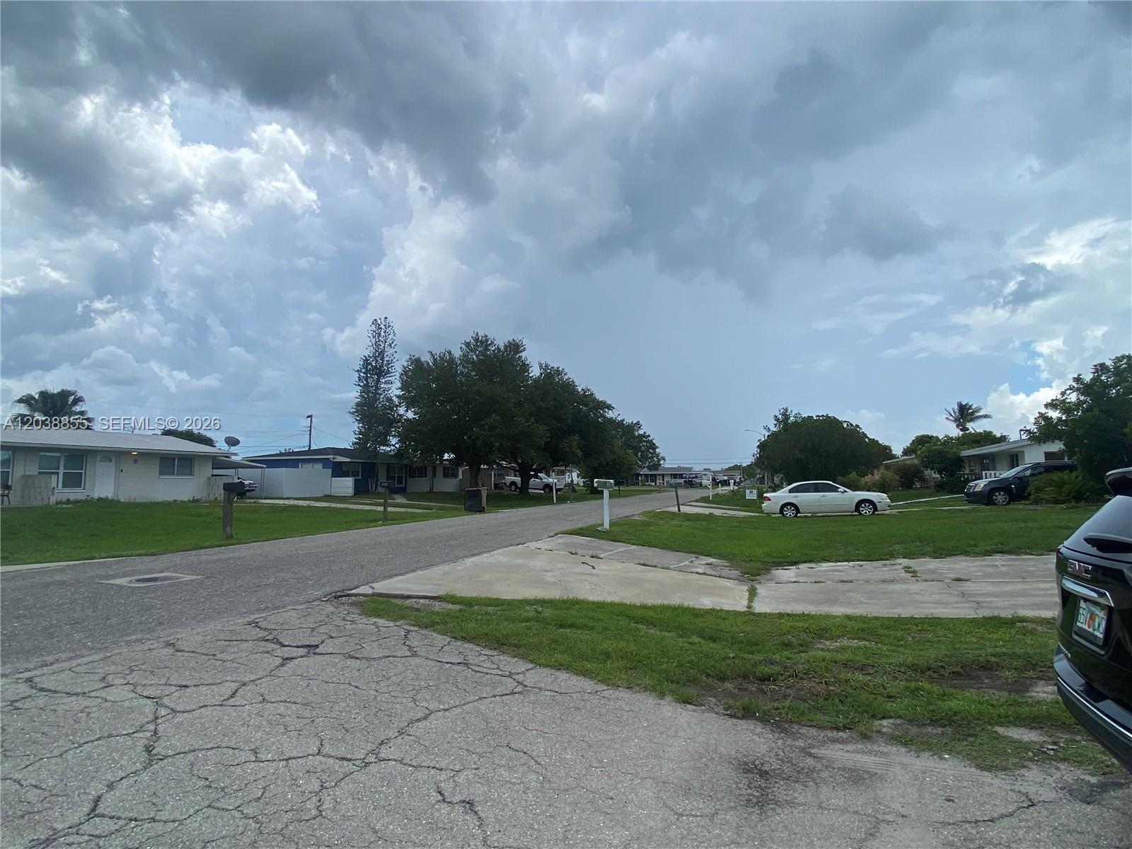 A residential street scene features houses, parked cars, and a cloudy sky — 1111 N VINEYARD ST, Lehigh Acres FL 33936, LEHIGH ACRES, FL