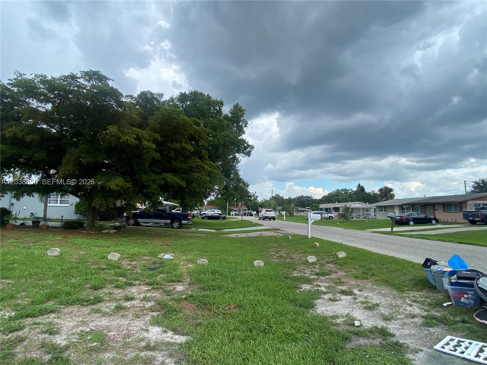 A residential street view features a grassy front yard, mature trees, and parked vehicles — 1111 N VINEYARD ST, Lehigh Acres FL 33936, LEHIGH ACRES, FL