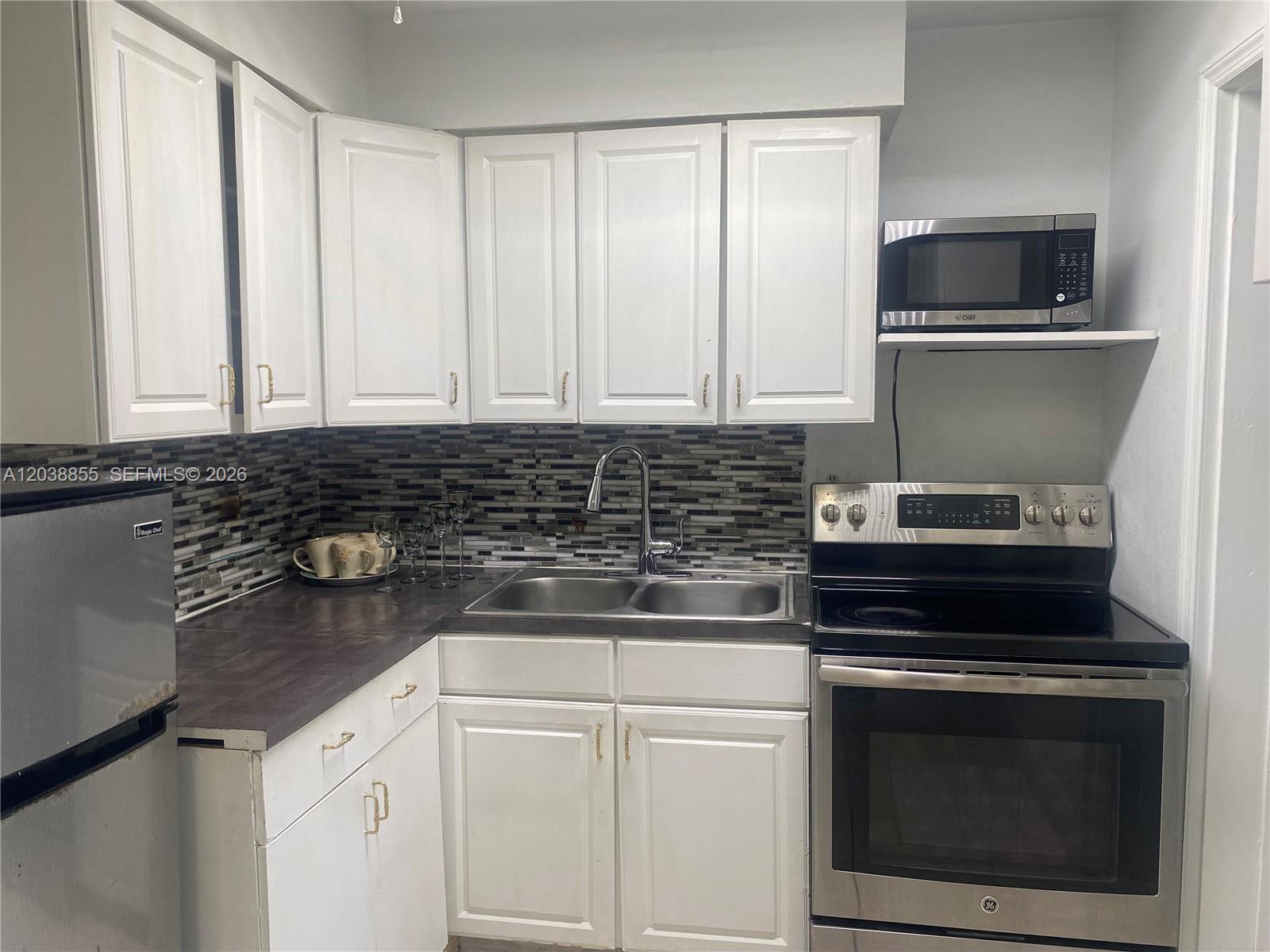 A kitchen features white cabinets, a dark countertop, stainless steel appliances, and a tiled backsplash — 1111 N VINEYARD ST, Lehigh Acres FL 33936, LEHIGH ACRES, FL