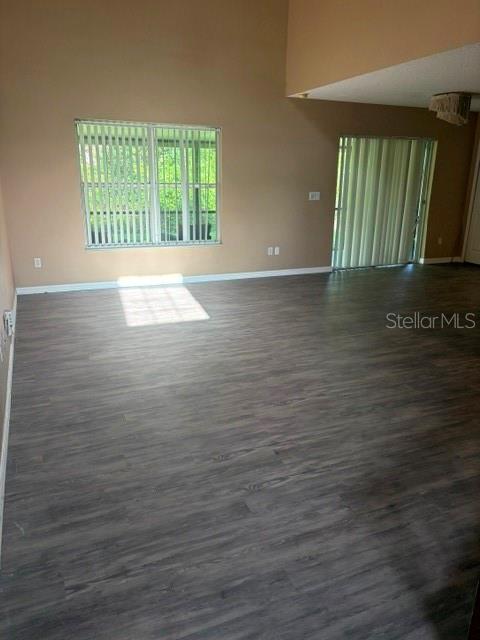 An empty room with vaulted ceilings, gray wood-look flooring, and vertical blinds on the windows — 2014 STONE ABBEY BOULEVARD, ORLANDO, FL