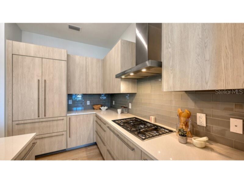 A modern kitchen features light wood cabinetry, a stainless steel range hood, and a tiled backsplash — 33 S PALM AVENUE UNIT 904, SARASOTA, FL
