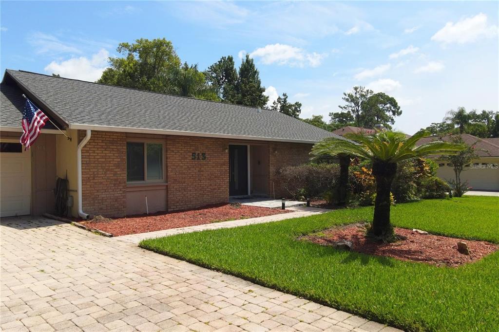A single-story brick house features a paved driveway, a front lawn, and a palm tree — 513 E WILDMERE AVENUE, LONGWOOD, FL