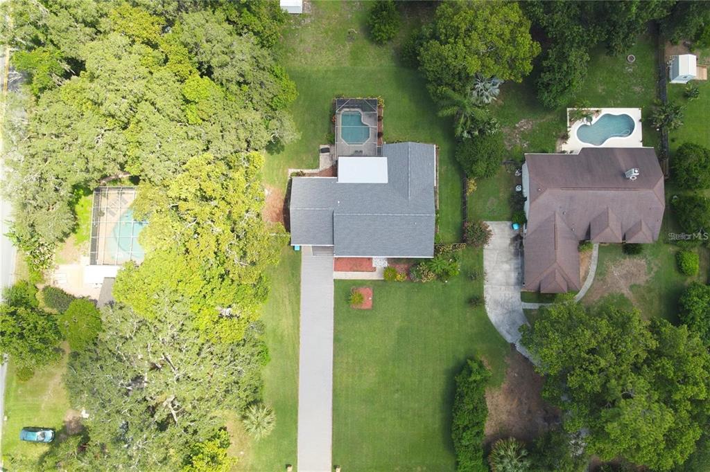 An aerial view shows a house with a pool and driveway surrounded by lush trees — 513 E WILDMERE AVENUE, LONGWOOD, FL