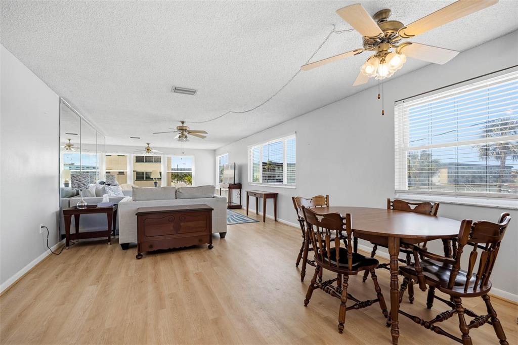 A living and dining room with light wood-look flooring, ceiling fans, and large windows — 2850 59TH STREET S UNIT 215, GULFPORT, FL