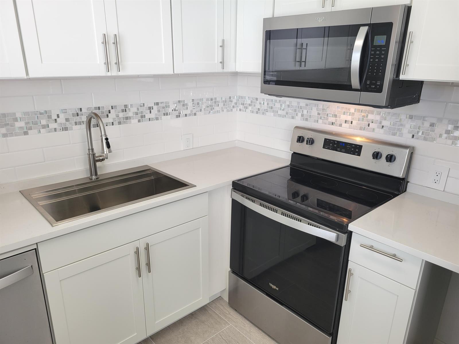 A kitchen featuring white cabinets, stainless steel appliances, a tile backsplash, and quartz countertops — 613 Fanshaw, Boca Raton FL 33434, BOCA RATON, FL