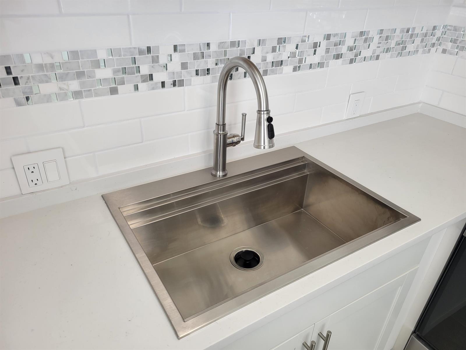 A stainless steel kitchen sink with a pull-down faucet is set in a white countertop — 613 Fanshaw, Boca Raton FL 33434, BOCA RATON, FL