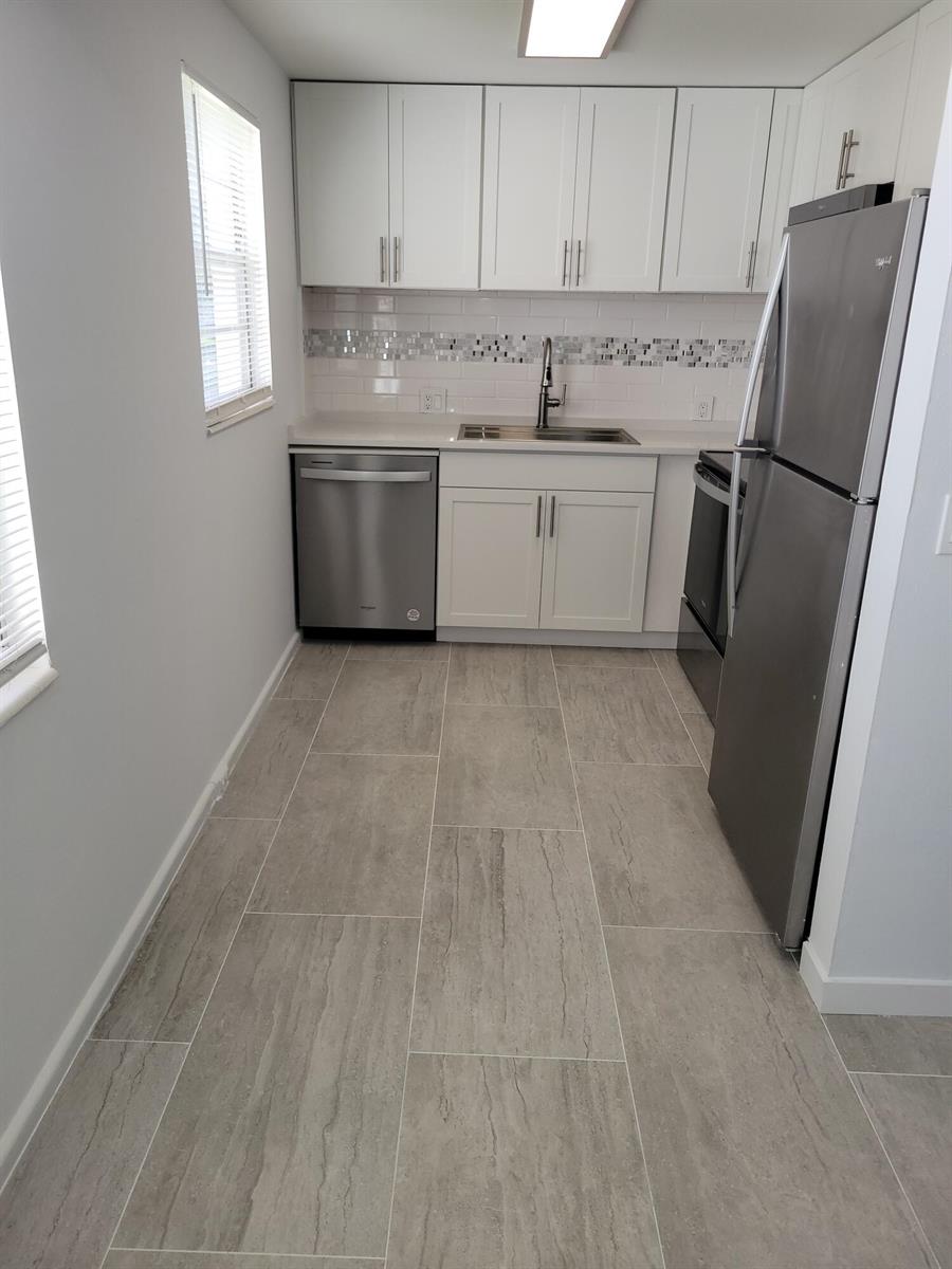 A galley kitchen features white cabinets, stainless steel appliances, a tiled backsplash, and gray flooring — 613 Fanshaw, Boca Raton FL 33434, BOCA RATON, FL