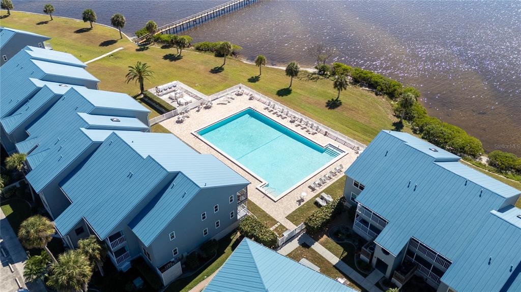 An aerial view shows a swimming pool surrounded by blue-roofed buildings near a waterfront — 4410 WARREN AVENUE UNIT 216, PORT CHARLOTTE, FL
