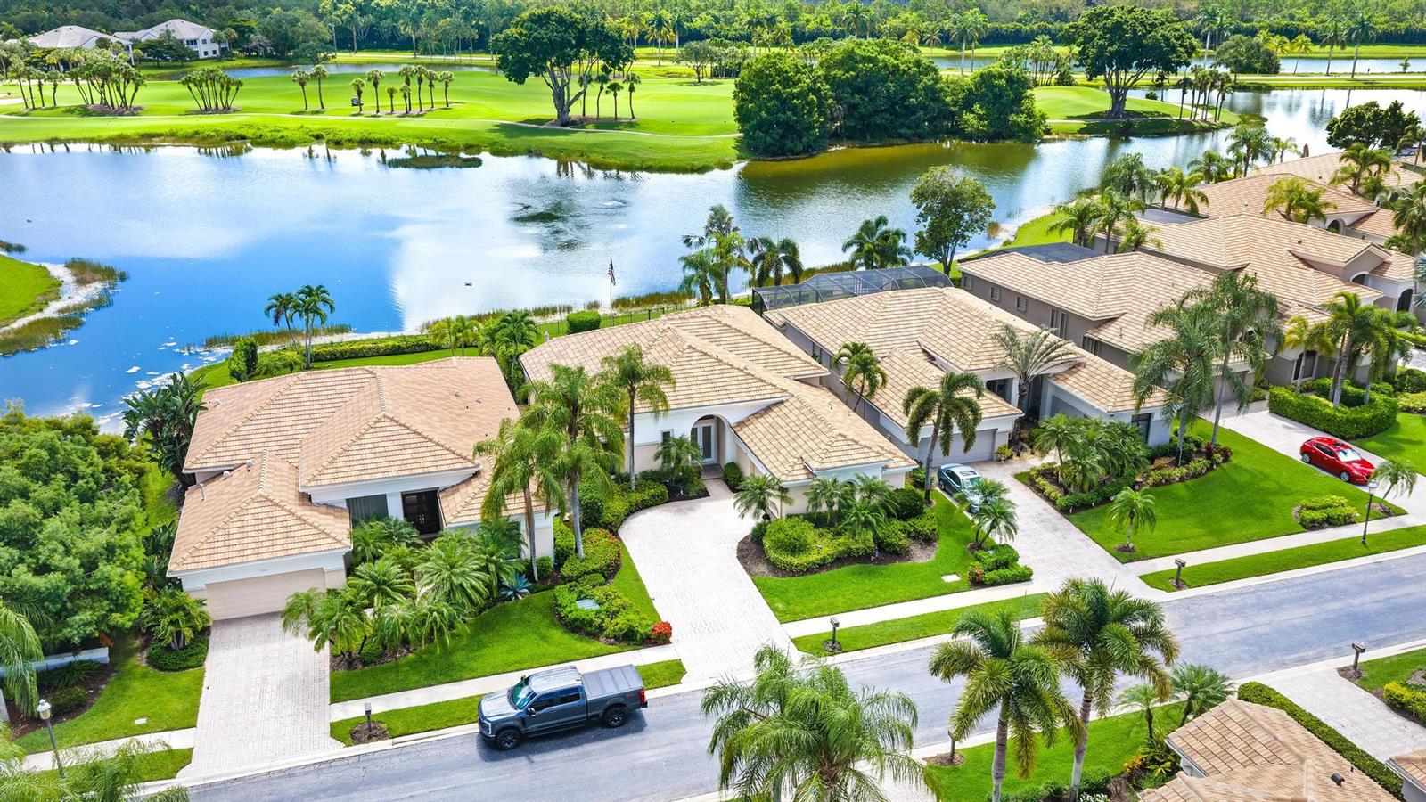 An aerial view shows several suburban houses with tiled roofs situated along a golf course lake — 7510 Blue Heron Way, West Palm Beach FL 33412, WEST PALM BEACH, FL