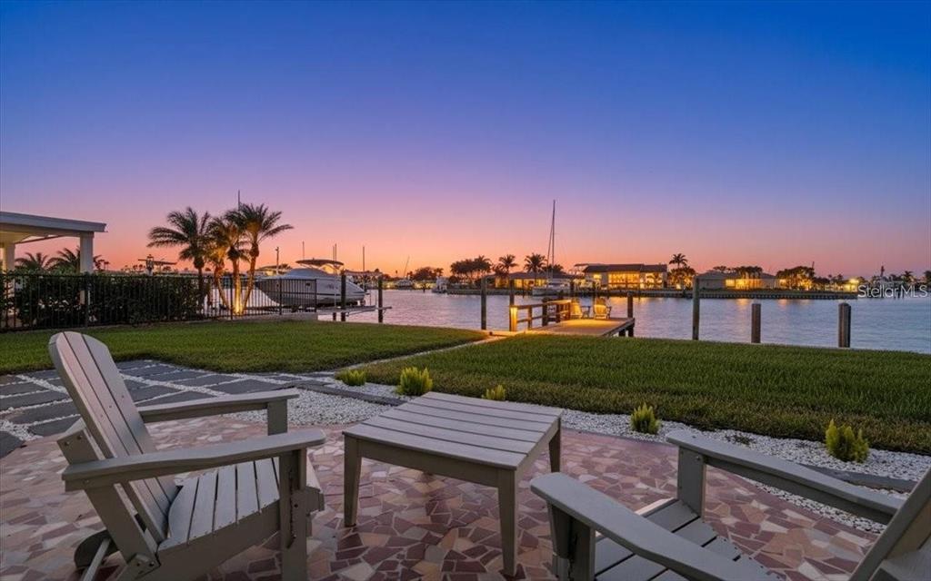 A patio with two chairs and a table overlooks a grassy lawn and a canal — 510 115TH AVENUE, TREASURE ISLAND, FL