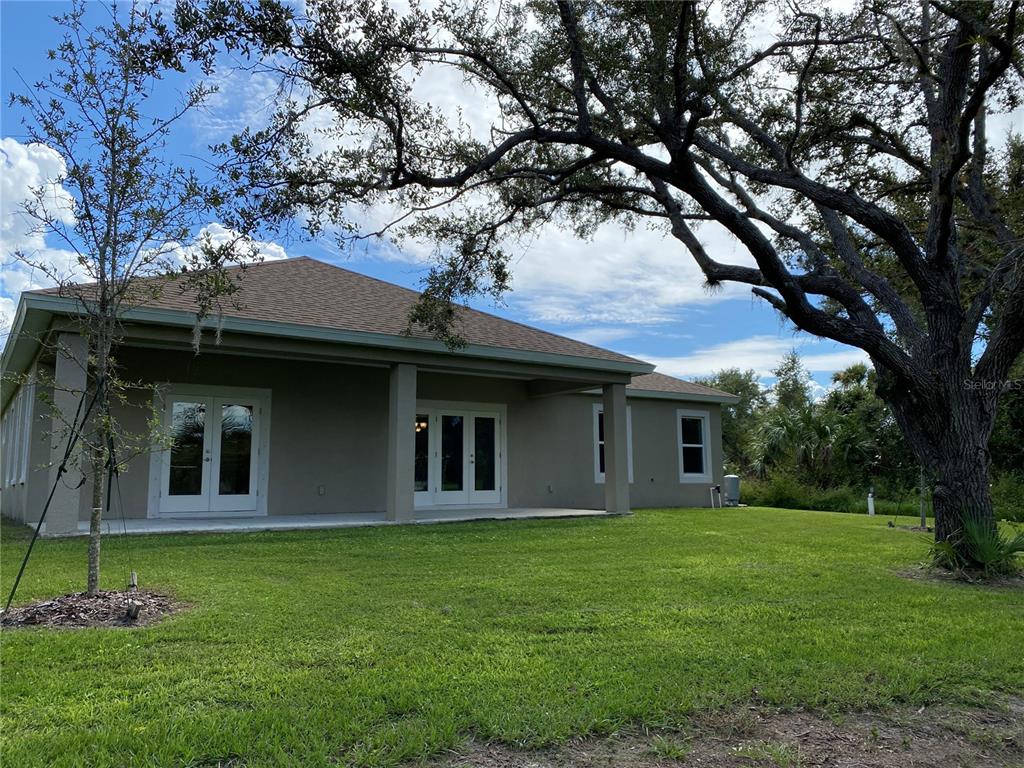 A view of the back of a house with a covered patio and large tree — 3481 NASHVILLE ROAD, NORTH PORT, FL