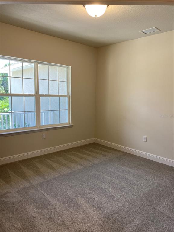 An empty bedroom features beige walls, gray carpeting, a large window, and a ceiling light — 3481 NASHVILLE ROAD, NORTH PORT, FL