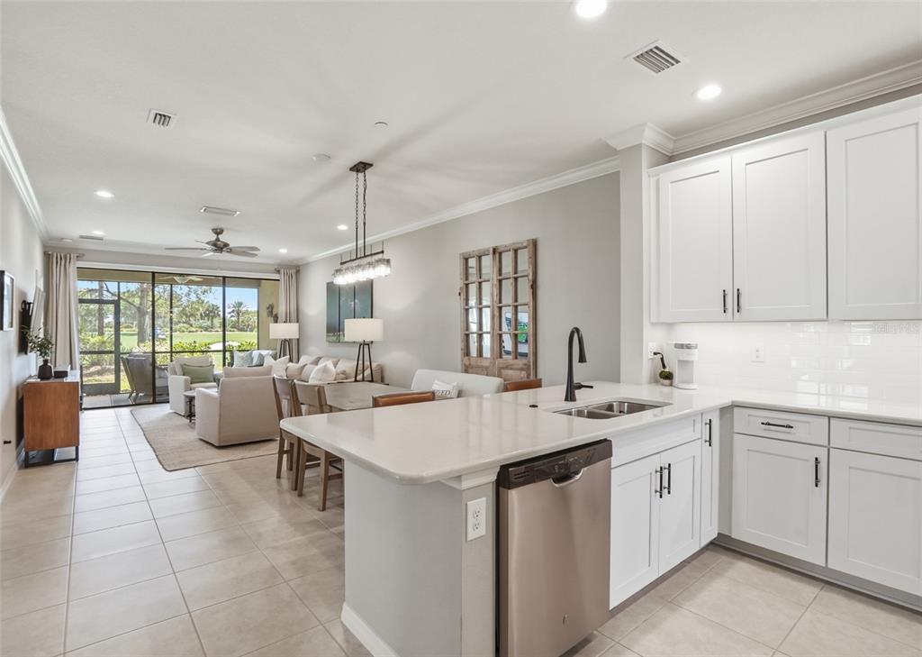 A kitchen with white cabinets and a stainless steel dishwasher overlooks an open-concept living area — 12720 SORRENTO WAY UNIT 101, BRADENTON, FL