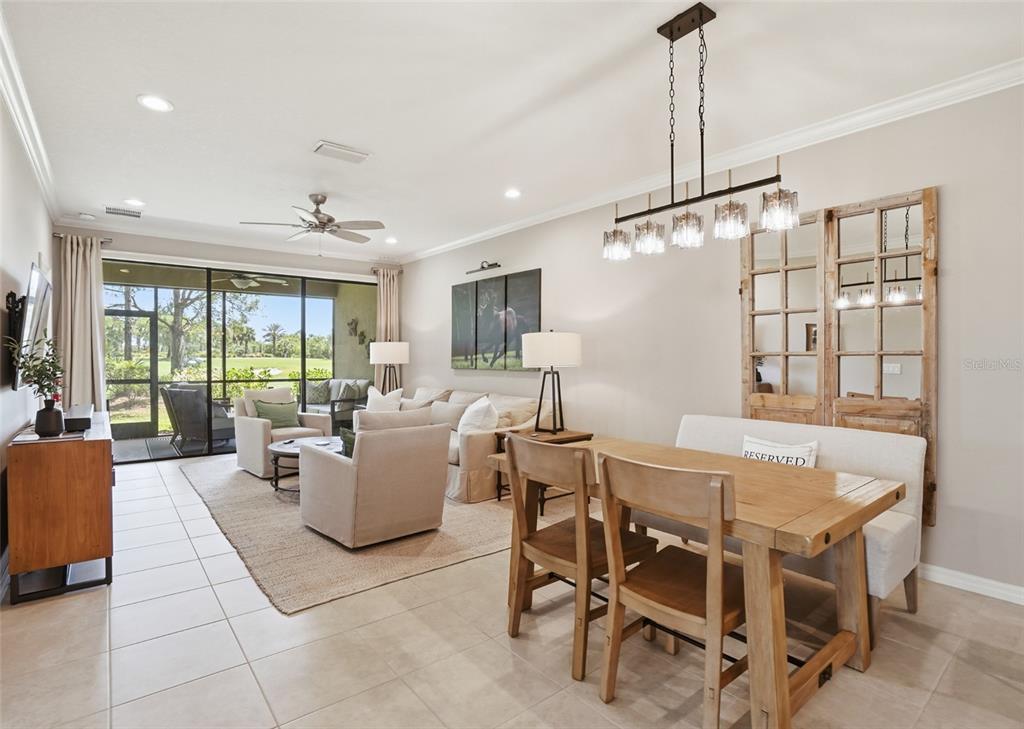 A living and dining area features tile floors, neutral furniture, and a view of greenery — 12720 SORRENTO WAY UNIT 101, BRADENTON, FL