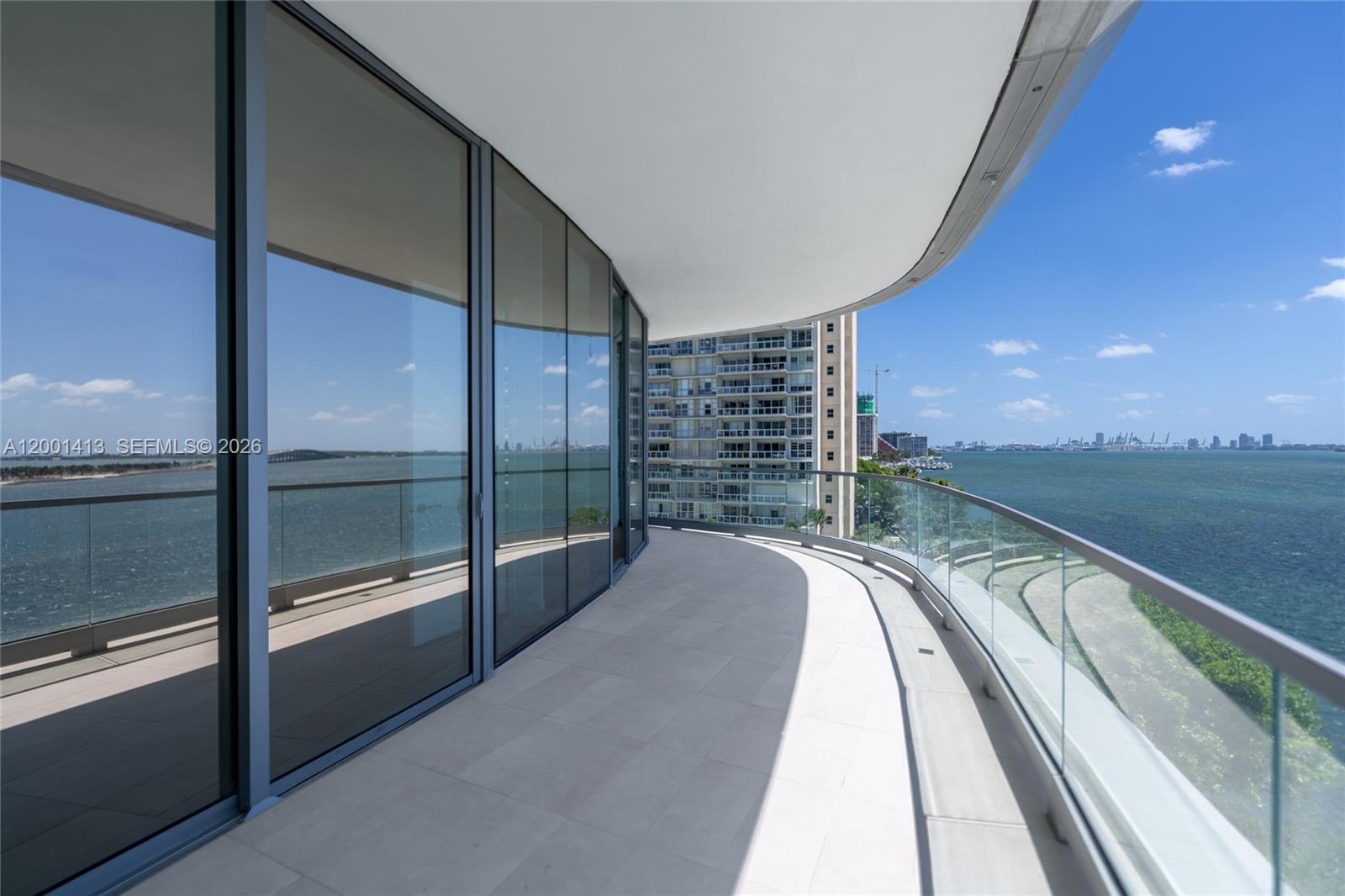 A curved balcony with glass railings overlooks the ocean and a neighboring high-rise building — 175 SE 25 Rd # 501, Miami FL 33129, MIAMI, FL