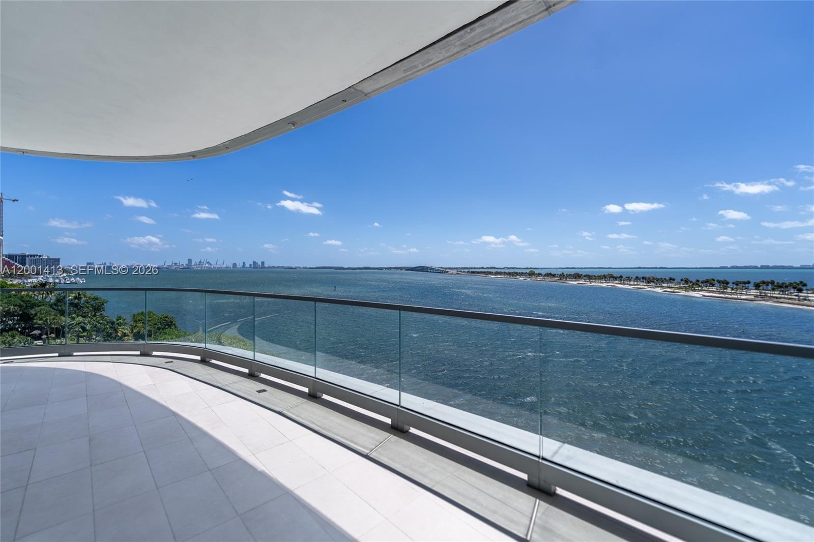 A curved balcony with a glass railing overlooks a large body of water and bridge — 175 SE 25 Rd # 501, Miami FL 33129, MIAMI, FL