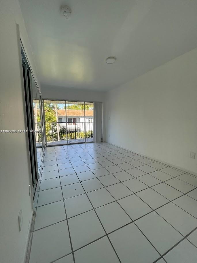 An empty room with white tile flooring, a mirrored closet, and a sliding glass door — 4271 NW 11th St # 1, Miami FL 33126, MIAMI, FL