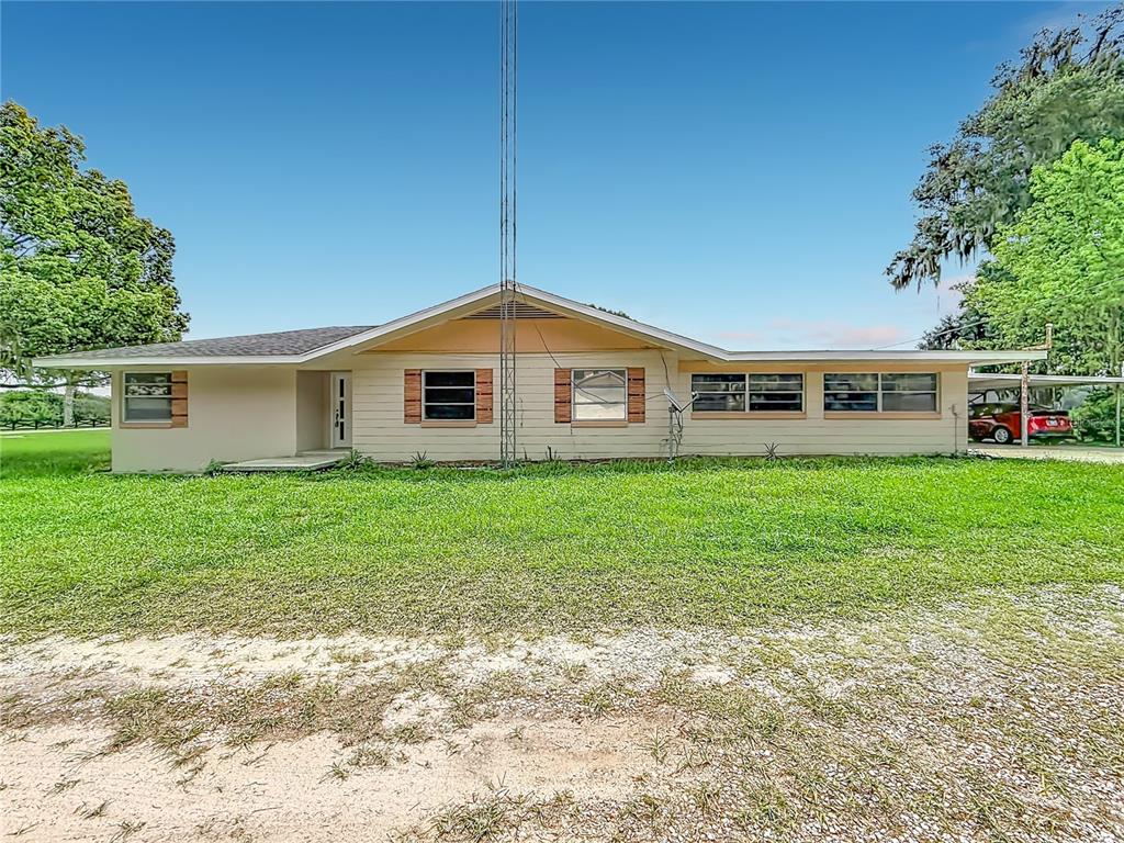 A single-story house with light-colored siding, a metal tower, and a gravel driveway — 11900 SE SUNSET HARBOR ROAD, WEIRSDALE, FL