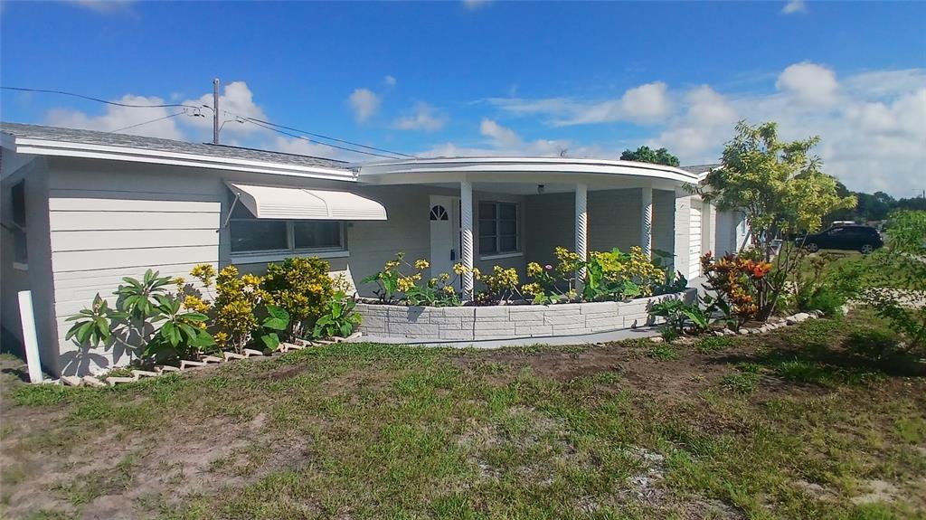 A single-story house with a curved front porch, white siding, and a landscaped stone planter — 2109 SHANNON DRIVE, HOLIDAY, FL