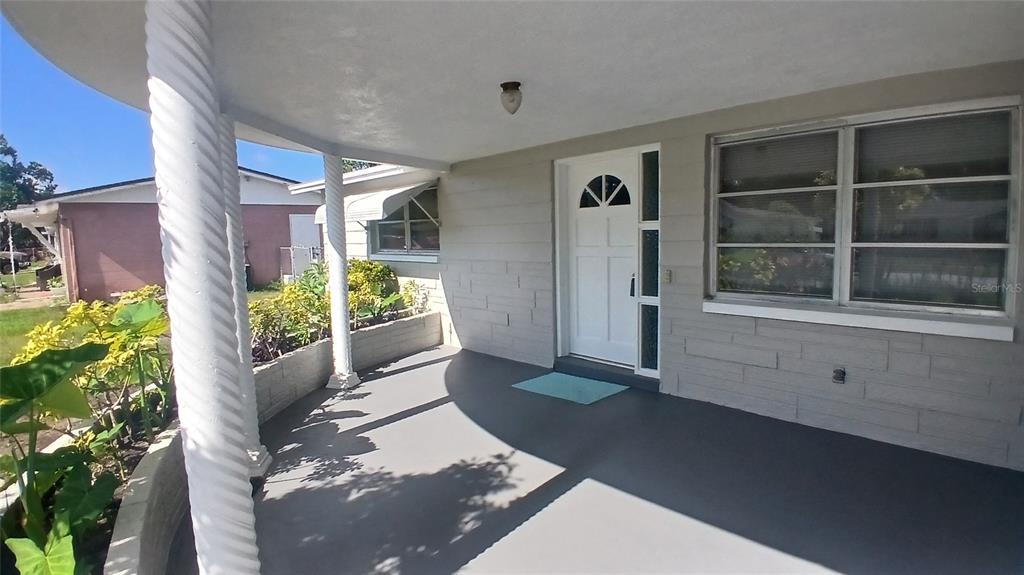 A covered front porch with white columns, a gray floor, and a white front door — 2109 SHANNON DRIVE, HOLIDAY, FL