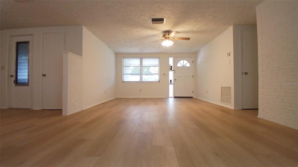 A living room features light wood-look flooring, white walls, a ceiling fan, and exterior doors — 2109 SHANNON DRIVE, HOLIDAY, FL