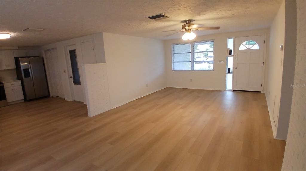 An open-concept living area features light wood-look flooring, a ceiling fan, and a white front door — 2109 SHANNON DRIVE, HOLIDAY, FL