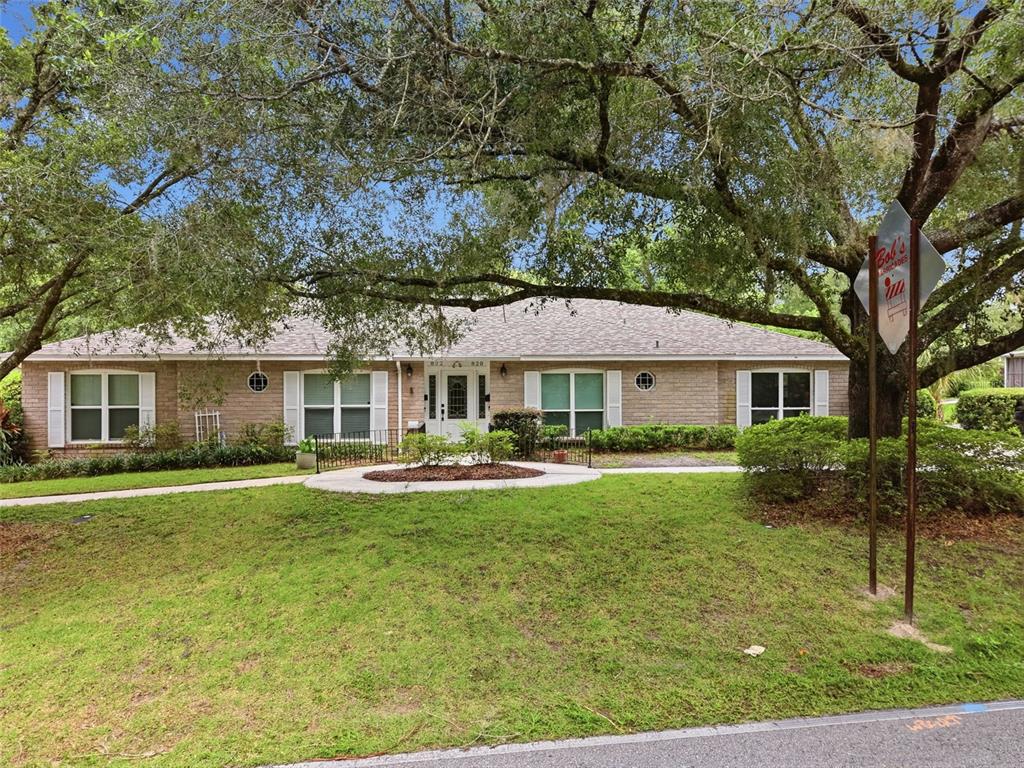 A single-story brick house with white shutters sits behind a grassy lawn and large trees — 820 S HILL AVENUE UNIT 40, DELAND, FL