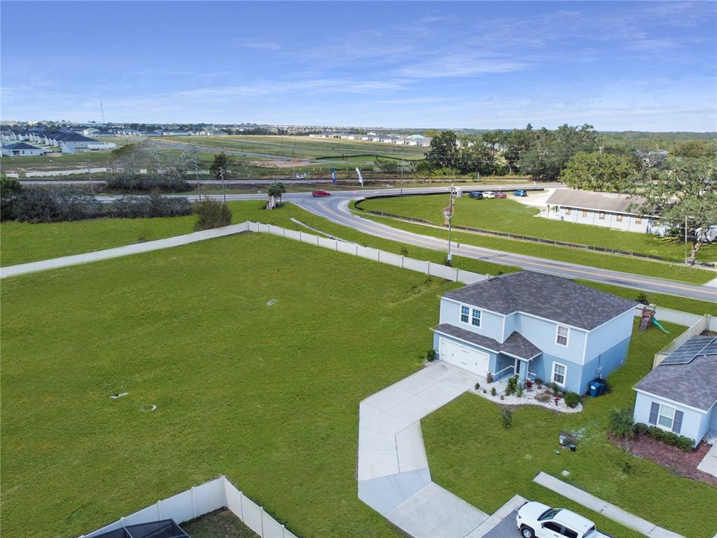An aerial view shows a two-story blue house next to a large, fenced vacant lot — 181 SILVER MAPLE BEND, DAVENPORT, FL