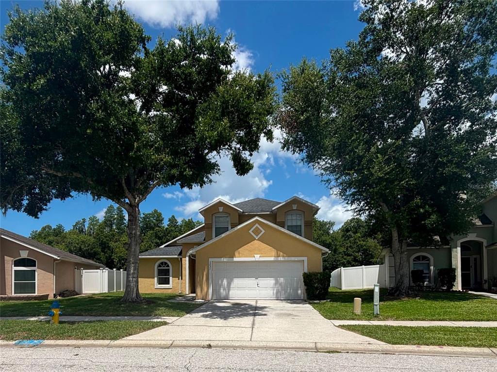 A two-story yellow house with a two-car garage and large trees in the front yard — 3231 CASTLE ROCK CIRCLE, LAND O LAKES, FL