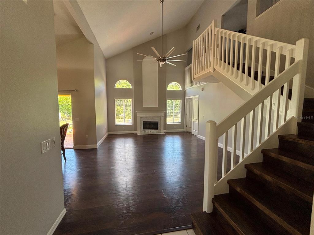 A living room features dark wood floors, a fireplace, and a staircase with white railings — 3231 CASTLE ROCK CIRCLE, LAND O LAKES, FL