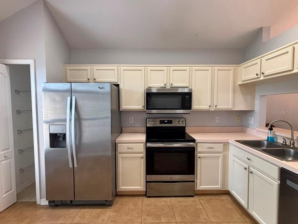 A kitchen features white cabinets, stainless steel appliances, pink countertops, and light tile flooring — 3231 CASTLE ROCK CIRCLE, LAND O LAKES, FL