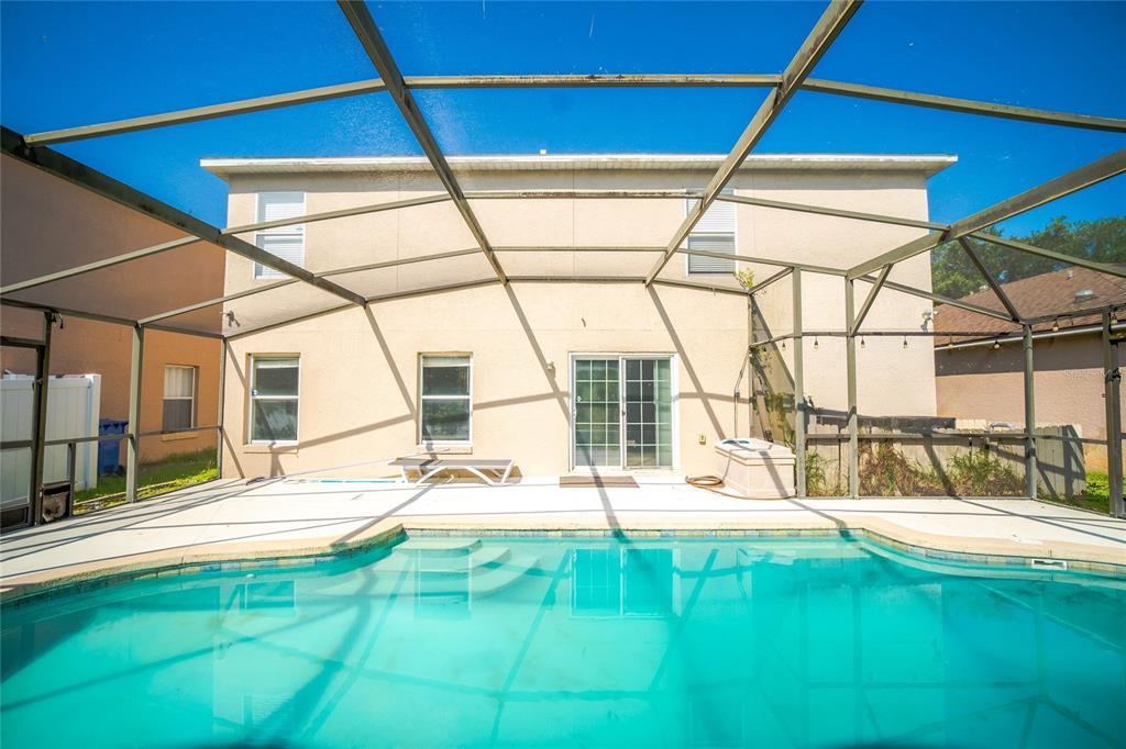 A swimming pool sits in a screened-in lanai behind a two-story beige stucco house — 381 AUGUSTINE COURT, OVIEDO, FL