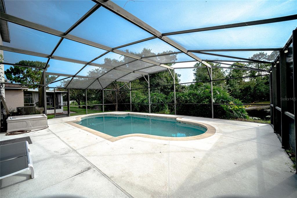 A screened-in patio features a kidney-shaped swimming pool and concrete decking overlooking a pond — 381 AUGUSTINE COURT, OVIEDO, FL